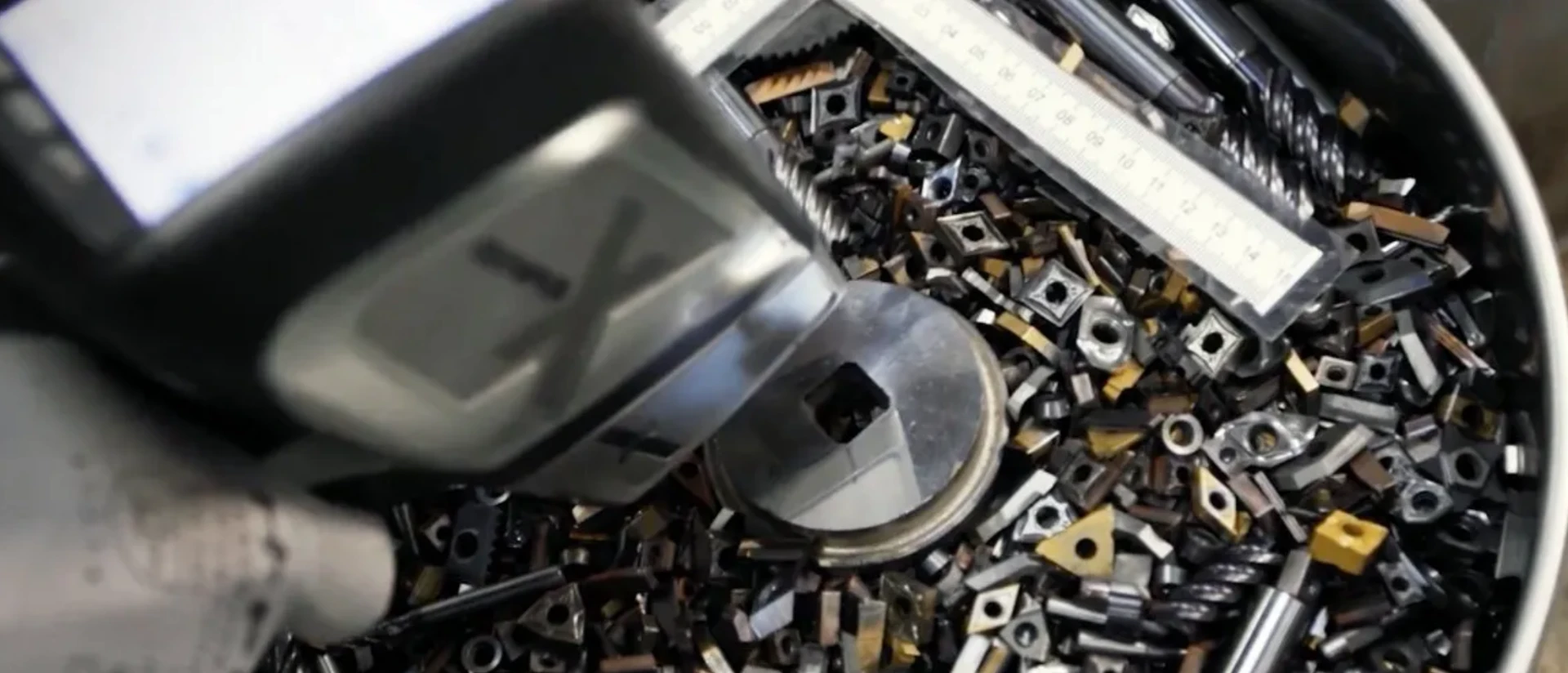 Bin of carbide inserts, end mills, and measuring tools being inspected in a machine shop.